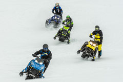 Snowmobilers riding along trail with helmet in foreground