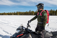 Snow patrol officer standing on snowmobiler looking over trails